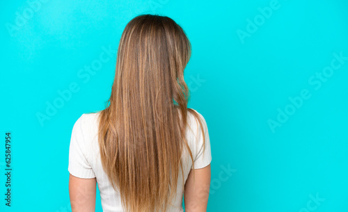 Young caucasian woman isolated on blue background in back position and looking side