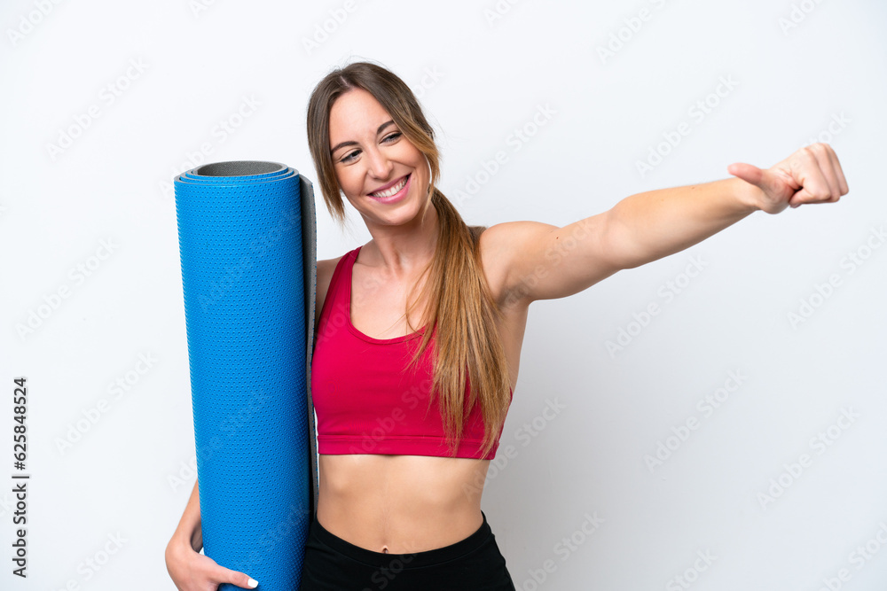 Young sport woman going to yoga classes while holding a mat isolated on white background giving a thumbs up gesture