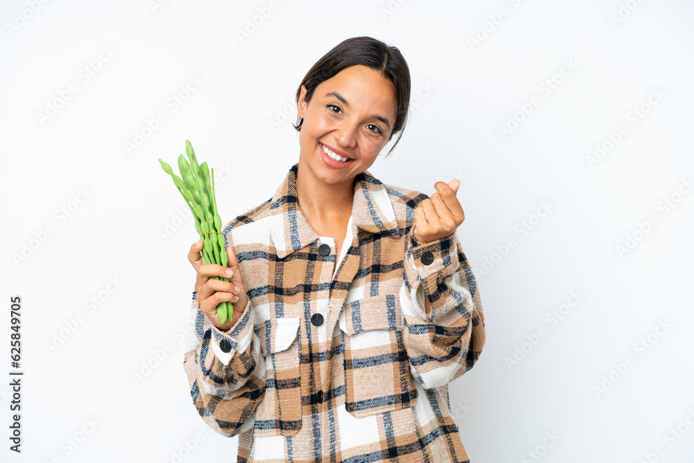Young hispanic woman holding a green beans isolated on white background making money gesture Young hispanic woman holding a green beans isolated on white background making money gesture