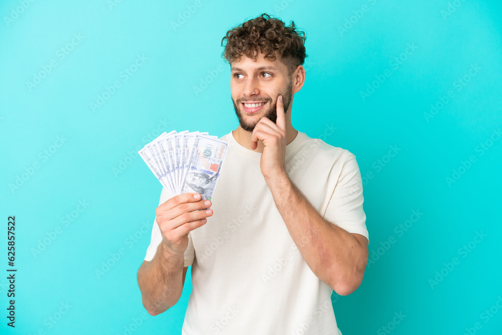 Young caucasian man taking a lot of money isolated on blue background thinking an idea while looking up Young caucasian man taking a lot of money isolated on blue background thinking an idea while looking up