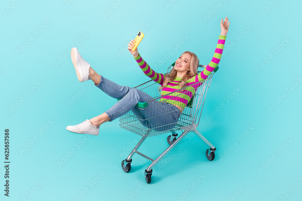 Full length photo of carefree pretty woman dressed sweater sitting shopping recording self video isolated turquoise color background Full length photo of carefree pretty woman dressed sweater sitting shopping recording self video isolated turquoise color background