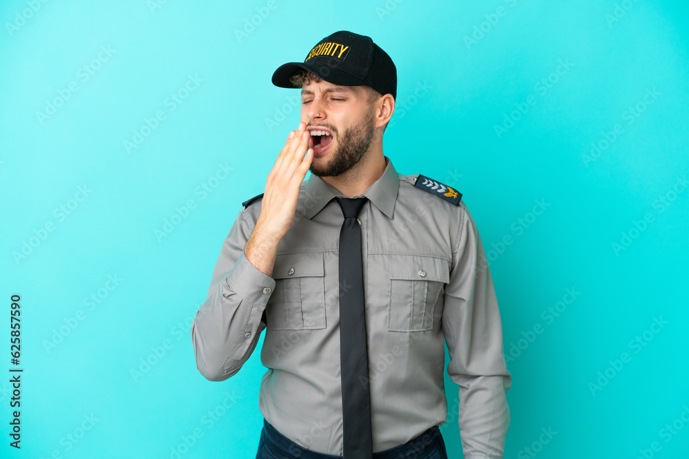 Young security man isolated on blue background yawning and covering wide open mouth with hand Young security man isolated on blue background yawning and covering wide open mouth with hand