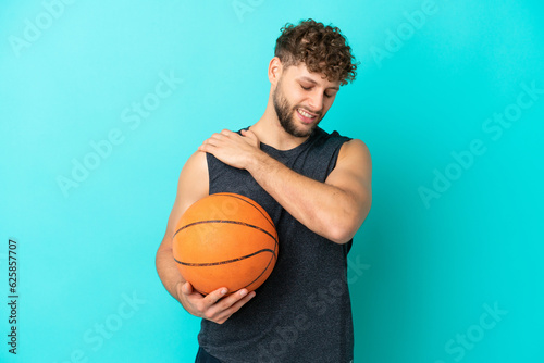 Handsome young man playing basketball isolated on blue background suffering from pain in shoulder for having made an effort