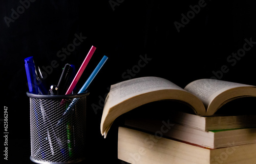 Close up shot of a pen stand with stationary items in it and pile of books with one opened -Higher Study concept. photo