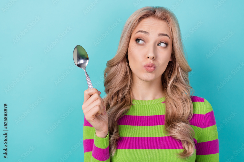 Photo of tricky cunning lady wear striped pullover rising spoon looking empty space isolated teal color background Photo of tricky cunning lady wear striped pullover rising spoon looking empty space isolated teal color background
