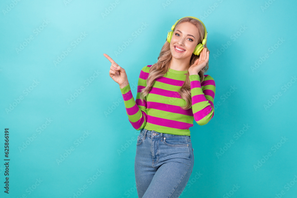 Photo of sweet shiny lady wear striped pullover listening songs earphones pointing empty space isolated teal color background Photo of sweet shiny lady wear striped pullover listening songs earphones pointing empty space isolated teal color background