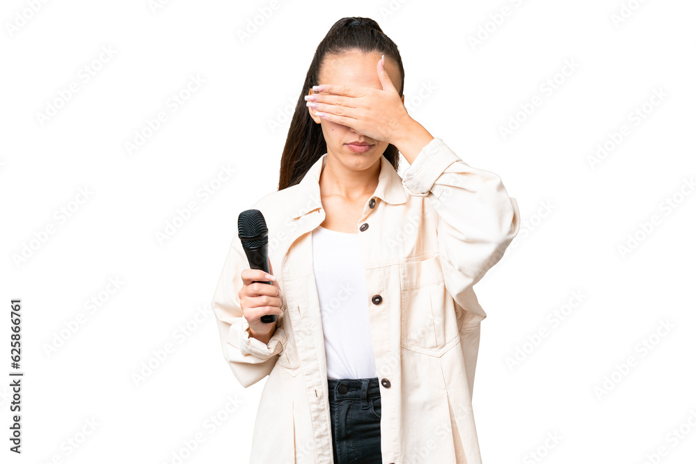 Young singer woman picking up a microphone over isolated chroma key background covering eyes by hands. Do not want to see something Young singer woman picking up a microphone over isolated chroma key background covering eyes by hands. Do not want to see something