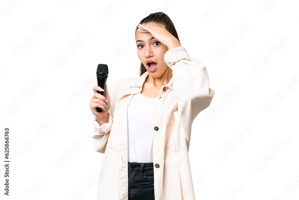Young singer woman picking up a microphone over isolated chroma key background doing surprise gesture while looking to the side Young singer woman picking up a microphone over isolated chroma key background doing surprise gesture while looking to the side