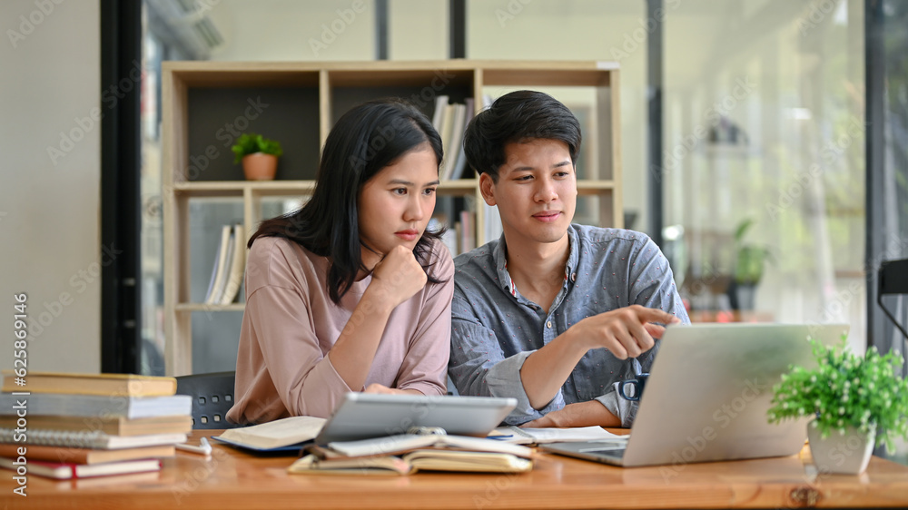 Two serious and focused Asian college students are looking at a laptop screen and discussing work Two serious and focused Asian college students are looking at a laptop screen and discussing work