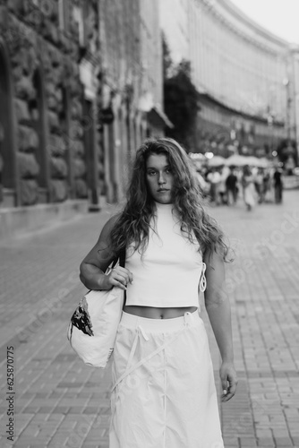 A trendy girl in a white outfit and curly hair on the city streets. © teksomolika