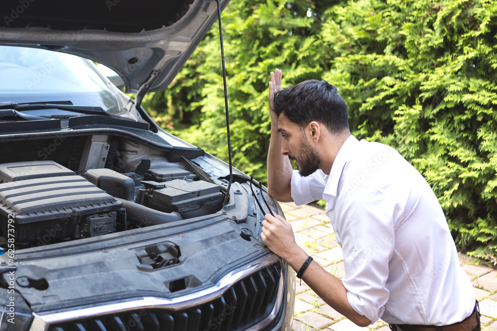 Shocked businessman stands in front of a broken car, opened the hood and tries to fix it Shocked businessman stands in front of a broken car, opened the hood and tries to fix it
