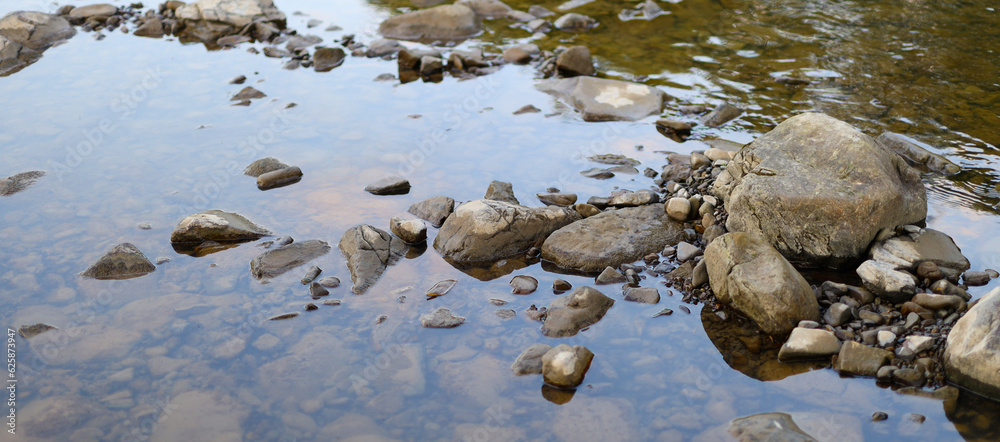 Obraz premium Rocky stream bed. The stream bed is filled with water and the water is clear. The rocks are various sizes and colors, ranging from small pebbles to larger boulders.