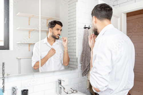 Handsome businessman brushing teeth in the bathroom. Morning routine concept