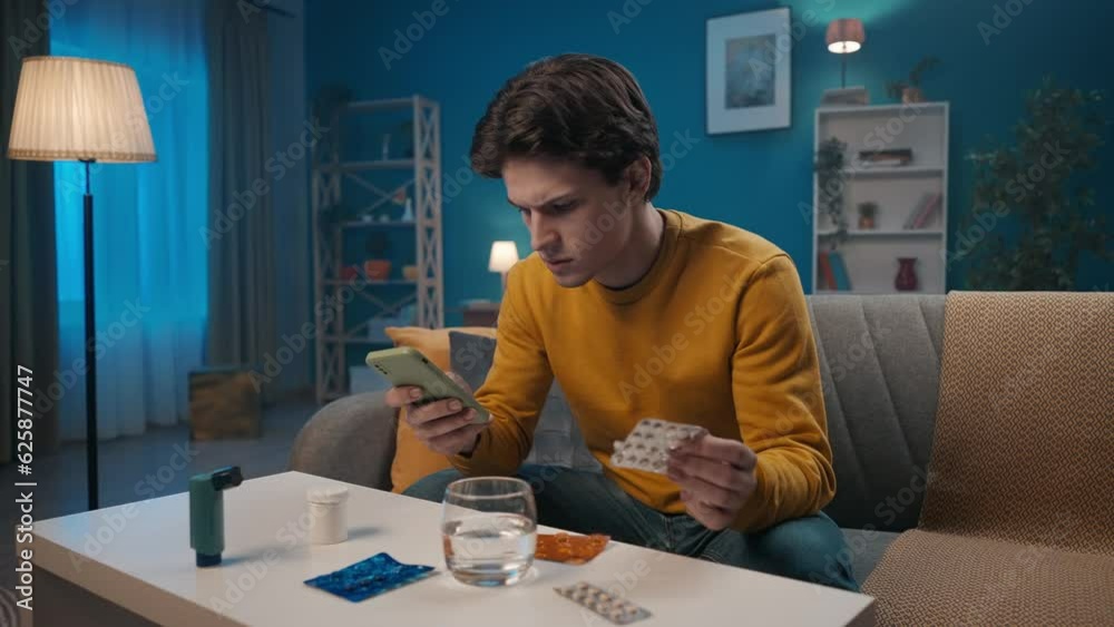 A man using a smartphone studies the instructions for taking pills. A sick man sits on a sofa in the living room, in front of him are medicines, a glass of water and an inhaler. Home medicine concept.
