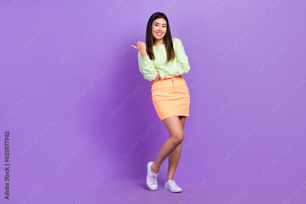 Portrait of satisfied gorgeous girl wear stylish pullover skirt indicating at offer empty space isolated on violet color background Portrait of satisfied gorgeous girl wear stylish pullover skirt indicating at offer empty space isolated on violet color background