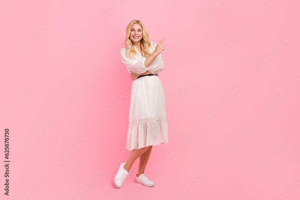 Full body photo of young woman wearing white trendy dress pointing finger empty space new promo brand isolated on pink color background Full body photo of young woman wearing white trendy dress pointing finger empty space new promo brand isolated on pink color background