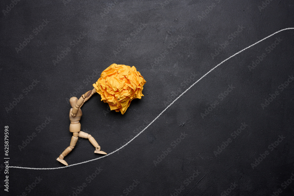 A wooden figurine of a person rolling a crumpled paper ball upwards, concept of perseverance and hard work, achieving goals. - obrazy, fototapety, plakaty 