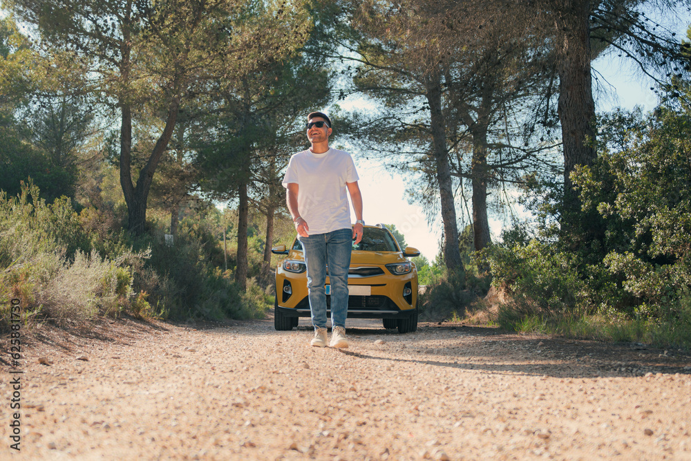 Latin man walking in a forest road with a yellow car in the background