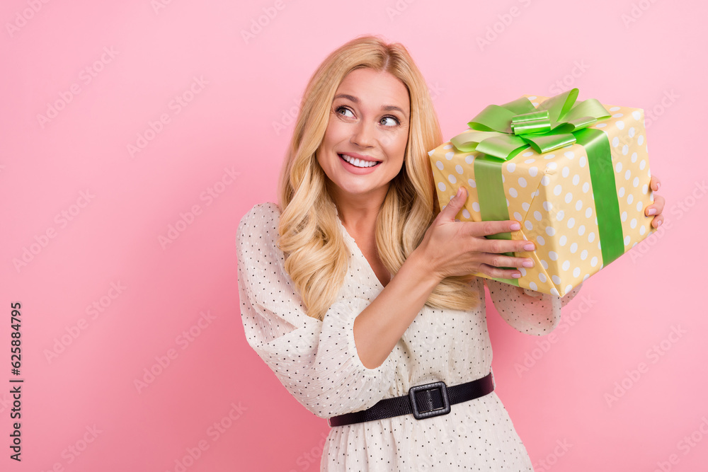 Photo portrait of attractive blonde woman hold present box look empty space dressed stylish white clothes isolated on pink color background Photo portrait of attractive blonde woman hold present box look empty space dressed stylish white clothes isolated on pink color background