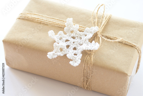 Christmas and New Year background. Gift box wrapped in kraft paper with jute cord. Decorated with a crocheted snowflake