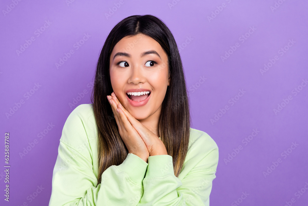 Photo of cute impressed lady wear green sweatshirt arms cheek looking empty space isolated purple color background Photo of cute impressed lady wear green sweatshirt arms cheek looking empty space isolated purple color background