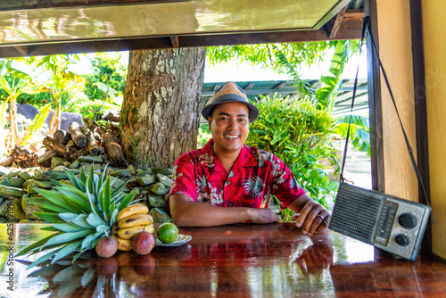 smiling young caribbean man dressed in flowery and tropical shirt and hat at outside bar