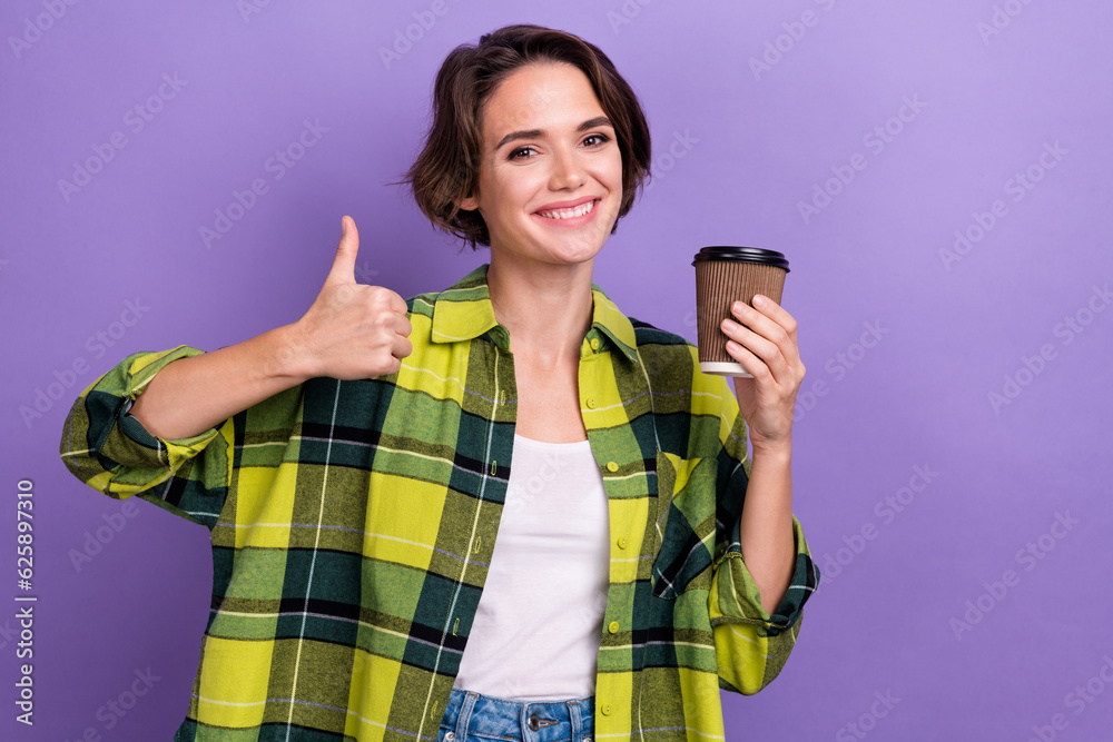 Portrait of charming cheerful girl toothy smile hold fresh coffee cup show thumb up empty space isolated on purple color background Portrait of charming cheerful girl toothy smile hold fresh coffee cup show thumb up empty space isolated on purple color background
