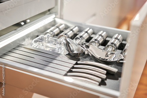 Kitchen utensil cutlery drawer organizer tray with simple set of tools, minimalist order. Open drawer with different utensils and folded towels. Order in kitchen. Kitchen furniture store.