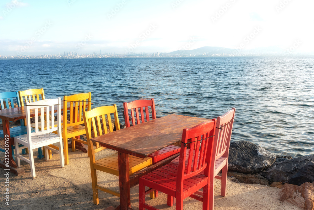 Soft morning light on coloured chairs and wooden tables set beside the sea on the Istanbul Island of Burgazada, party of the archipelago known as the Adalar in the Sea of Marmara, Turkey.