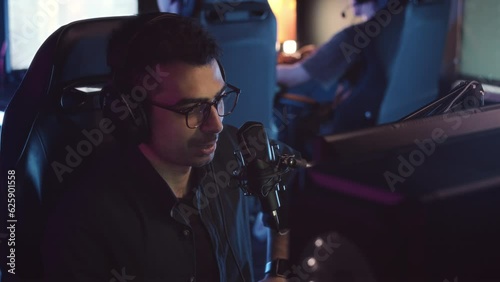 Waist up slowmo of Middle Eastern male streamer speaking in microphone while watching online PC game play at night cybersport clubWaist up slowmo of Middle Eastern male streamer speaking in microphone photo