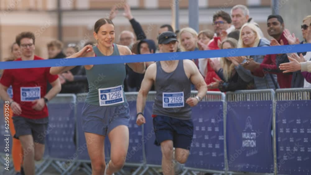 Slow Motion Portrait of Athletic Female Jogger Crossing the Finish Line in Marathon Race with the Audience Cheering. Happy Successful Woman Celebrating Winning, Feeling Empowered with her Achievement