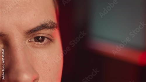 Closeup of brown eye of male gamer looking at computer screen while playing in dark room photo