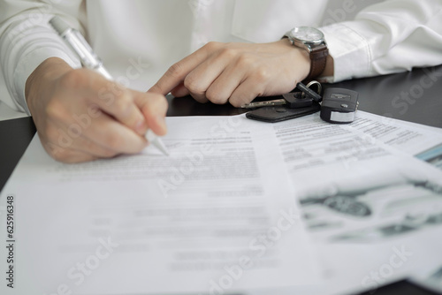 Man signing car insurance document or lease paper. Writing signature on contract or agreement. Buying or selling new or used vehicle. Car keys on wooden table. Warranty or guarantee.