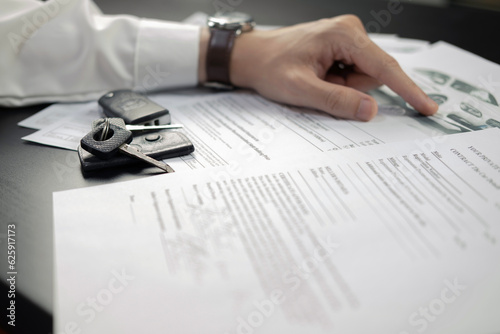 Man signing car insurance document or lease paper. Writing signature on contract or agreement. Buying or selling new or used vehicle. Car keys on wooden table. Warranty or guarantee.