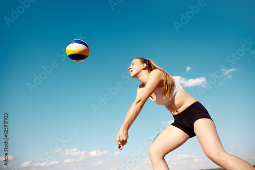 Young athletic women playing beach volleyball on warm summer day outdoors. Hitting ball with hands. Concentration. Concept of sport, active and healthy lifestyle, hobby, summertime, ad