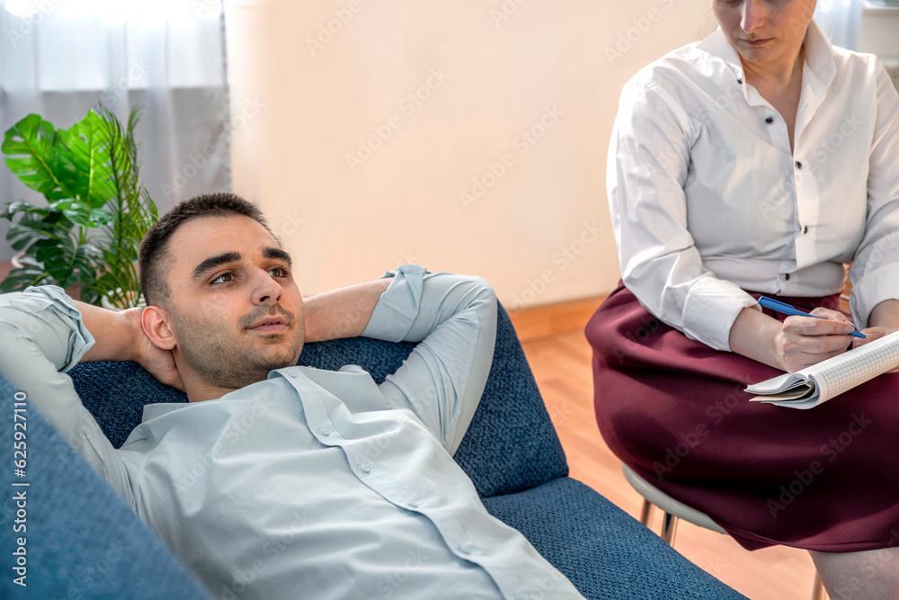 Obraz premium Session with a psychologist, psychotherapist. Young depressed male patient and professional female doctor with note pad. Lifestyle. Mental health care