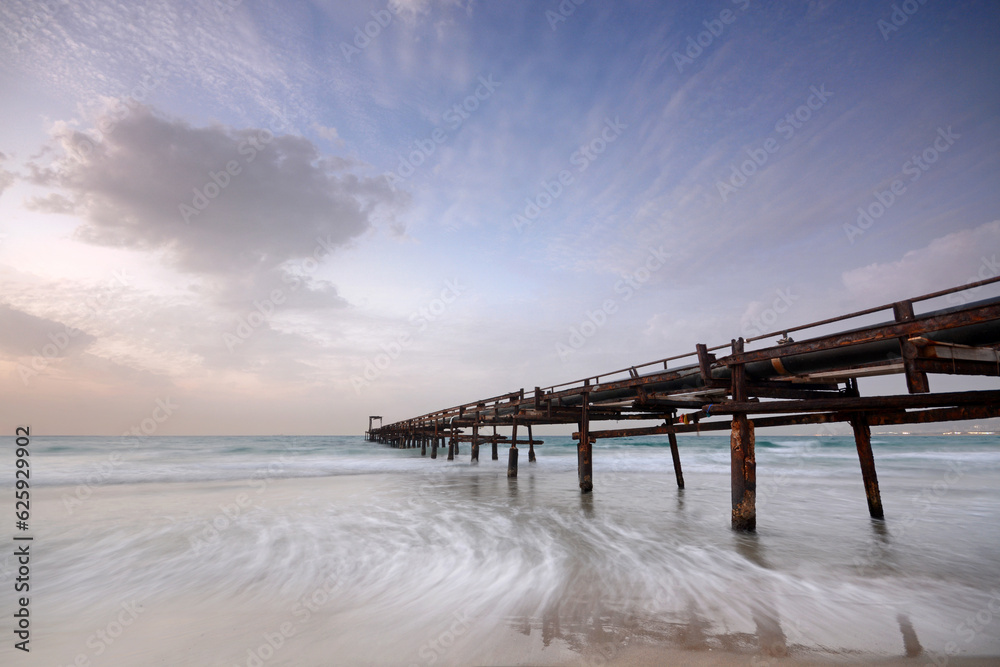 A look at a pier during sunset from below with soft waves and soft clouds
