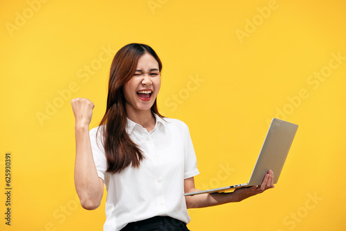 Young asian woman wearing white short sleeve shirt and holding laptop to working while smiling and raising