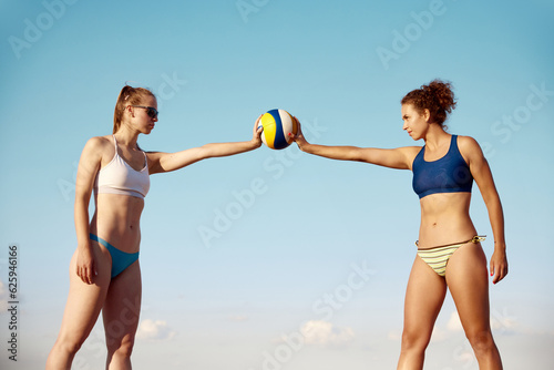 Two sportive young womsn, with fit, slim body in swimsuit holding volleyball ball over blue sky background. Concept of sport, active and healthy lifestyle, hobby, summertime, ad #625946166