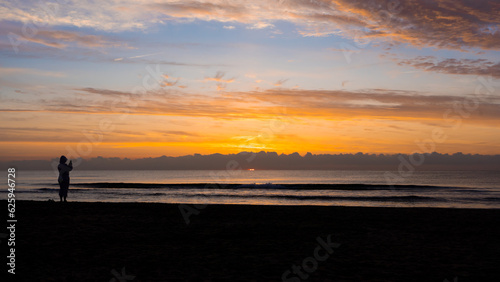Silhouette of woman taking photo. General plane. Spectacular landscape. Beautiful sunrise. Sea. Sun. Sand. Clouds