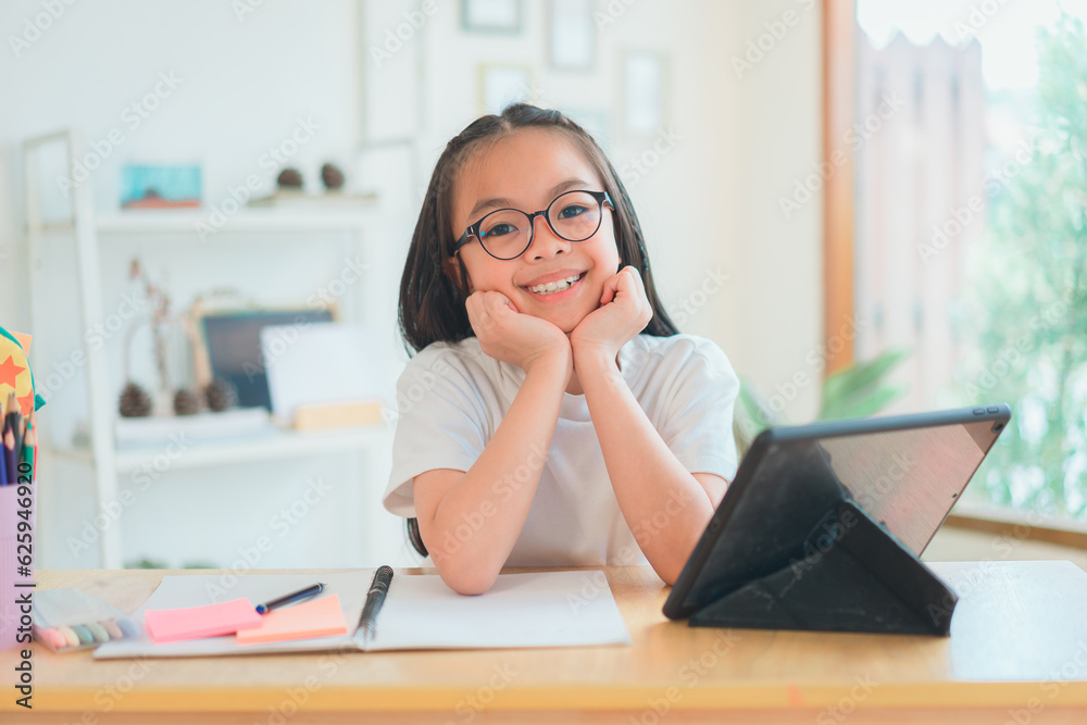 Asian school girl doing homework at laptop raising hand pointing finger . The girl does his homework. Home schooling. Asian school girl doing homework at laptop raising hand pointing finger . The girl does his homework. Home schooling.