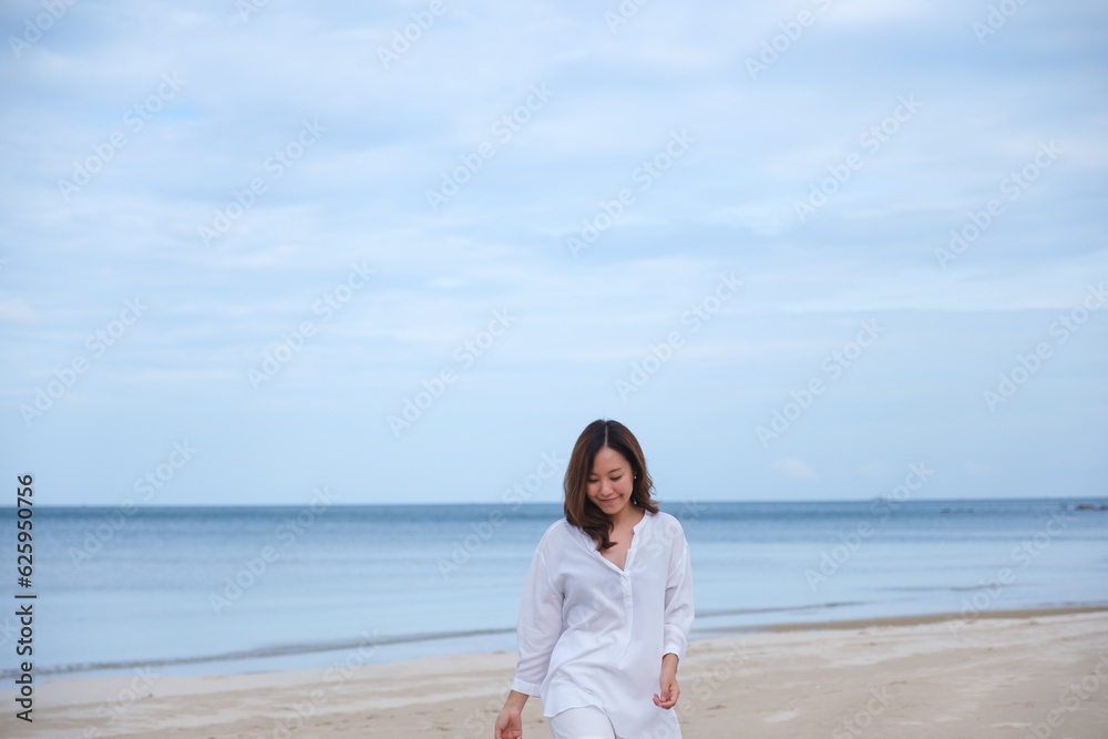 Portrait image of a beautiful young asian woman while strolling on the beach with the sea and blue sky Portrait image of a beautiful young asian woman while strolling on the beach with the sea and blue sky