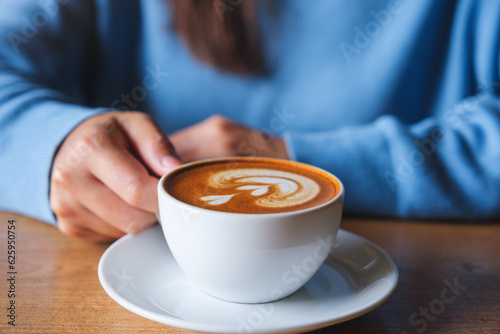 Closeup image of a woman holding a cup of latte coffee on wooden table
