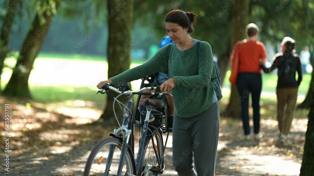 Fototapeta premium Happy mother and child outside carrying bike toddler in bicycle back seat