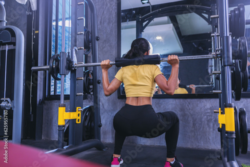 Fit young woman holding her hands with a weight barbell for pulling, squatting, workout in the fitness gym.