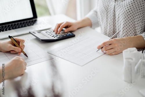 Two accountants using a calculator and laptop computer for counting taxes at white desk in office. Teamwork in business audit and finance
