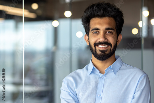 Εκτύπωση καμβά Portrait of a young Indian male student standing in an office, campus, library wearing a blue shirt and smiling at the camera