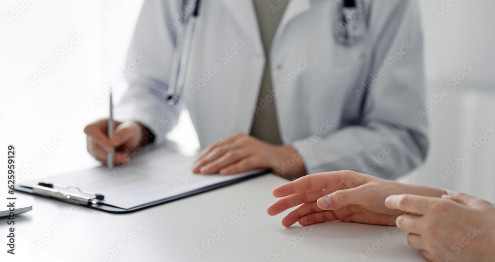 Doctor and patient discussing current health examination while sitting at the desk in clinic office. The focus is on female patient's hands, close up. Perfect medical service and medicine concept