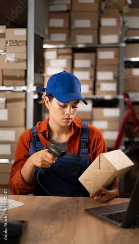 Female worker in warehouse using bar code scanner to scanning box sitting at the table. Working at warehouse. Export business concept