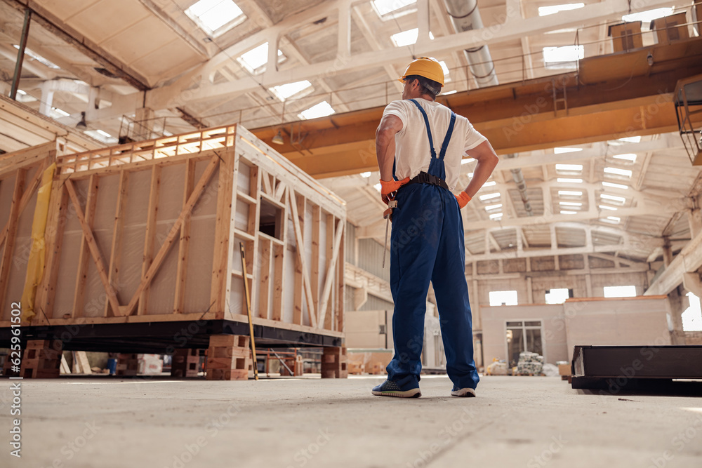 Fototapeta premium Male builder in work overalls observing building under construction